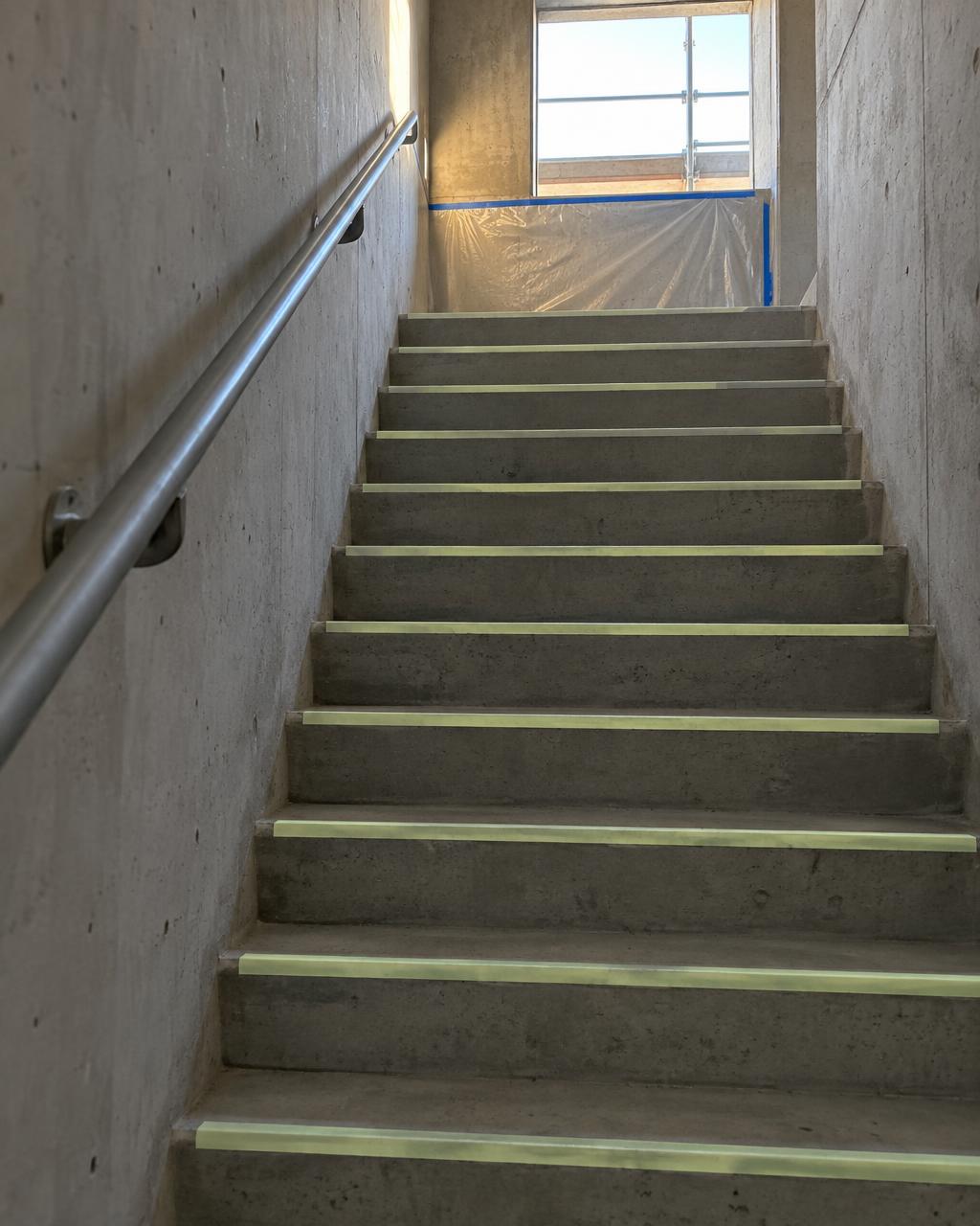Worker installing a photoluminescent egress strip on a stair nosing